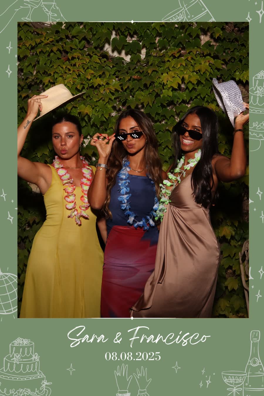 Impressão de photobooth de casamento: três convidadas com chapéus de palha e colares de flores, sobre um muro de hera, numa moldura verde-sálvia ilustrada com bolo e champanhe.